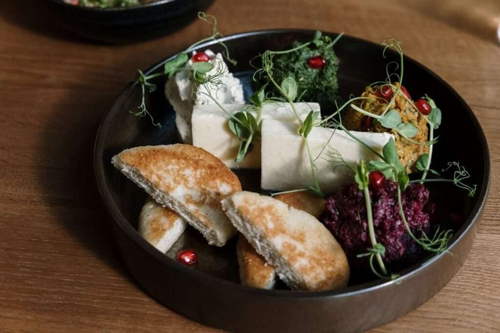 A gourmet platter featuring cheese, flatbread, dips, and garnished with fresh greens.